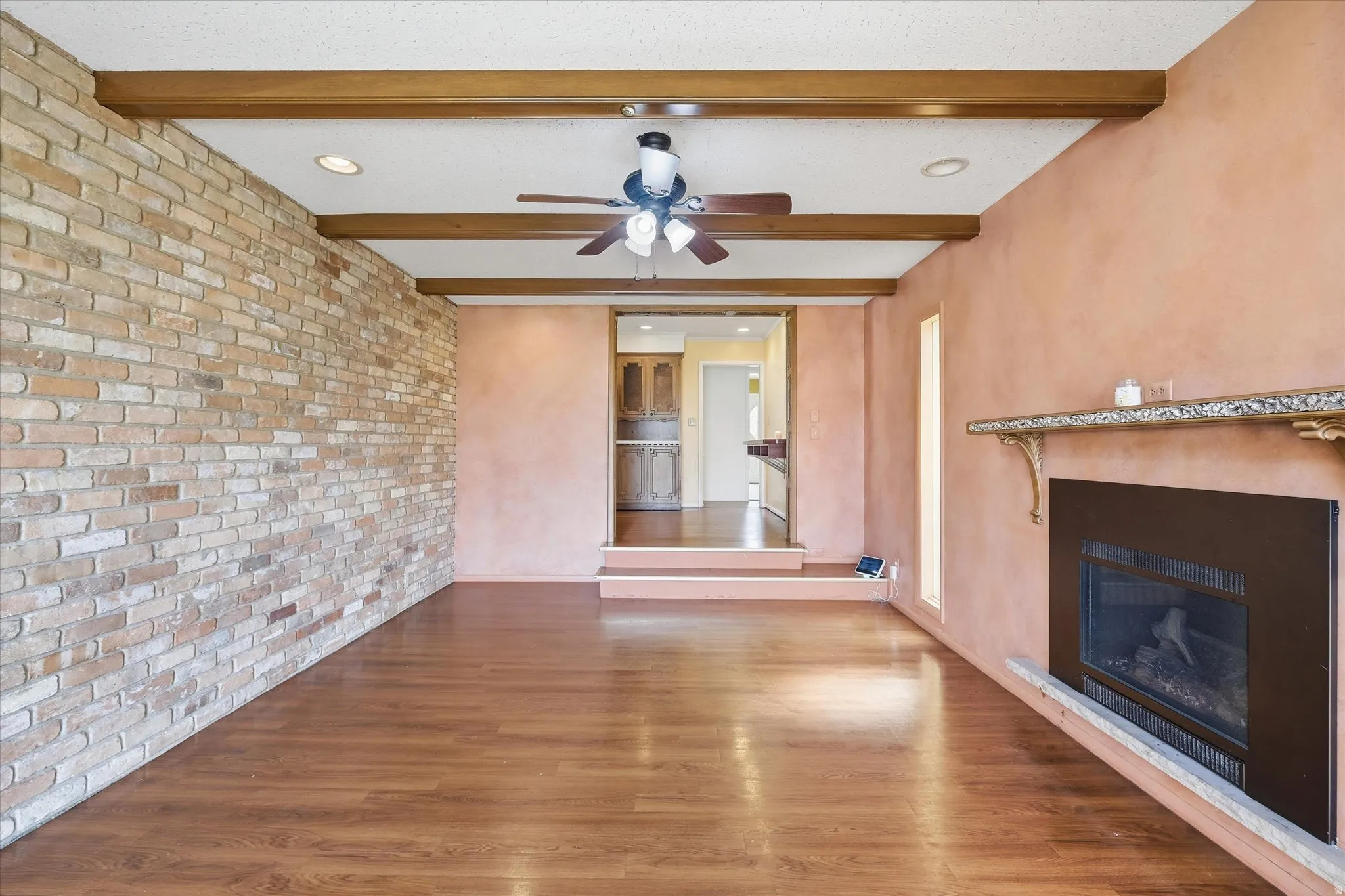 Spacious living area featuring wood-finish flooring, a full brick accent wall, and exposed wood ceiling beams