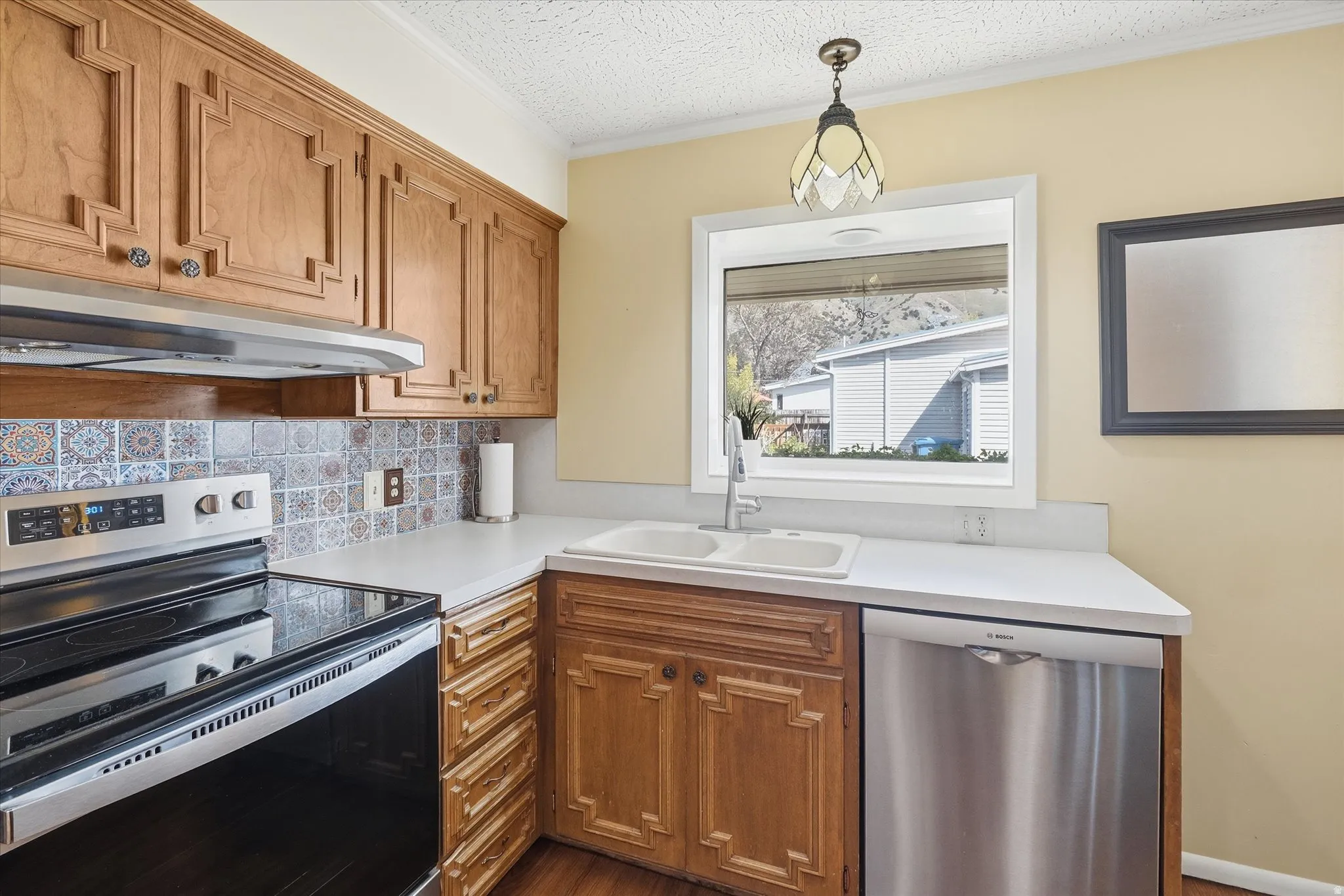 Kitchen featuring wood cabinetry, patterned tile backsplash, stainless steel appliances, and a window above the sink