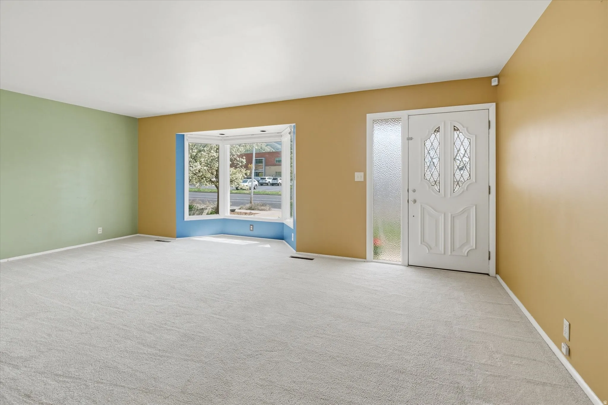 Spacious reception area featuring a decorative front door with opaque glass panels, a full-length sidelight, and a broad bay window