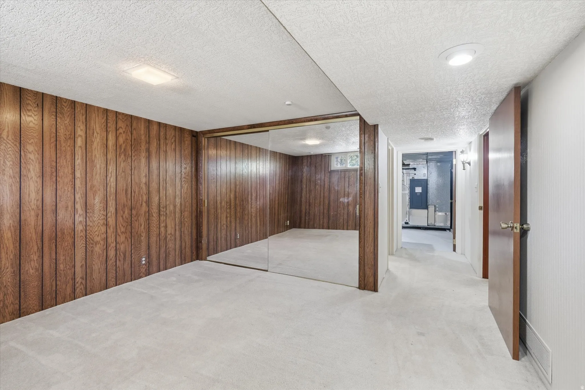 Spacious room featuring wood paneling, full-height mirrored wall, and soft carpeting
