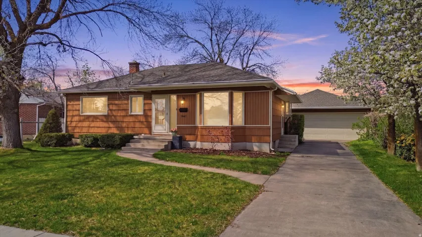 Ranch-style residence featuring warm-toned siding, a well-maintained front lawn, and mature trees