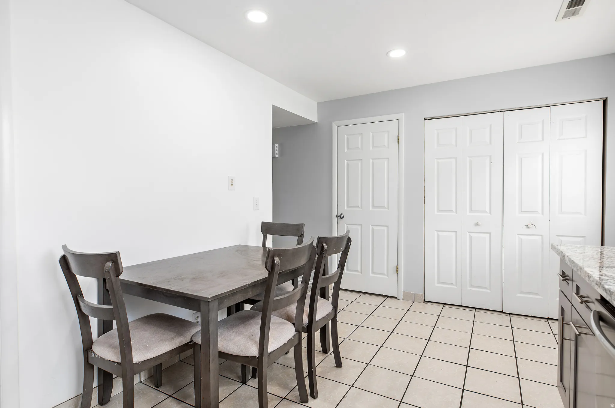 Spacious dining area featuring neutral wall colors, recessed lighting, white six-panel doors, and square tile flooring