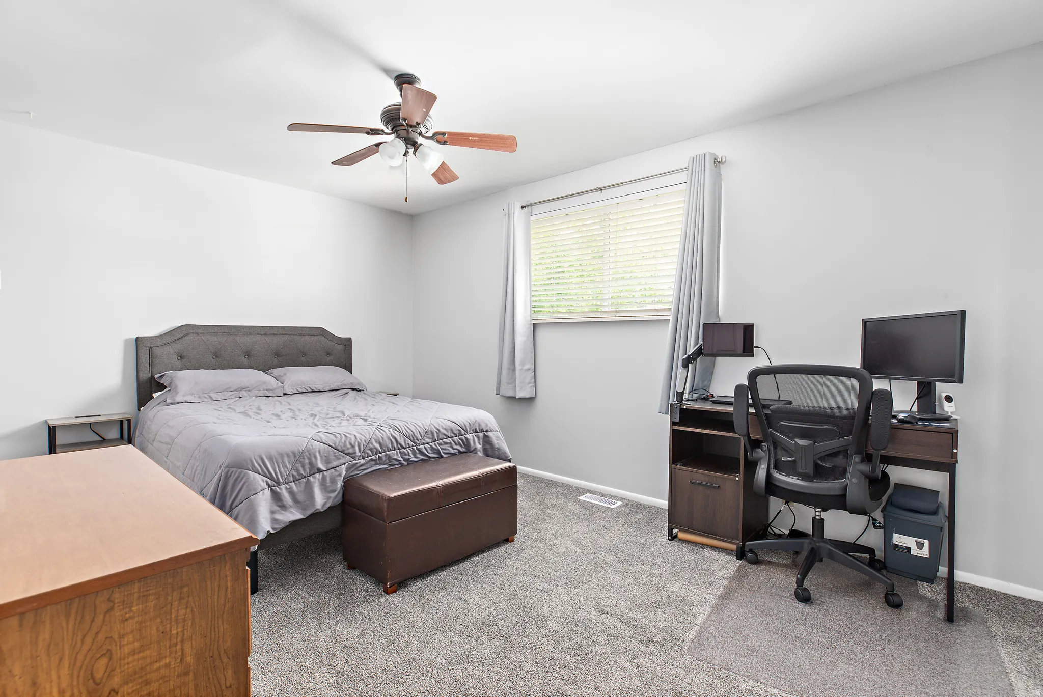 Carpeted bedroom with a window featuring blinds and drapes, a ceiling fan with integrated lighting, and light gray walls