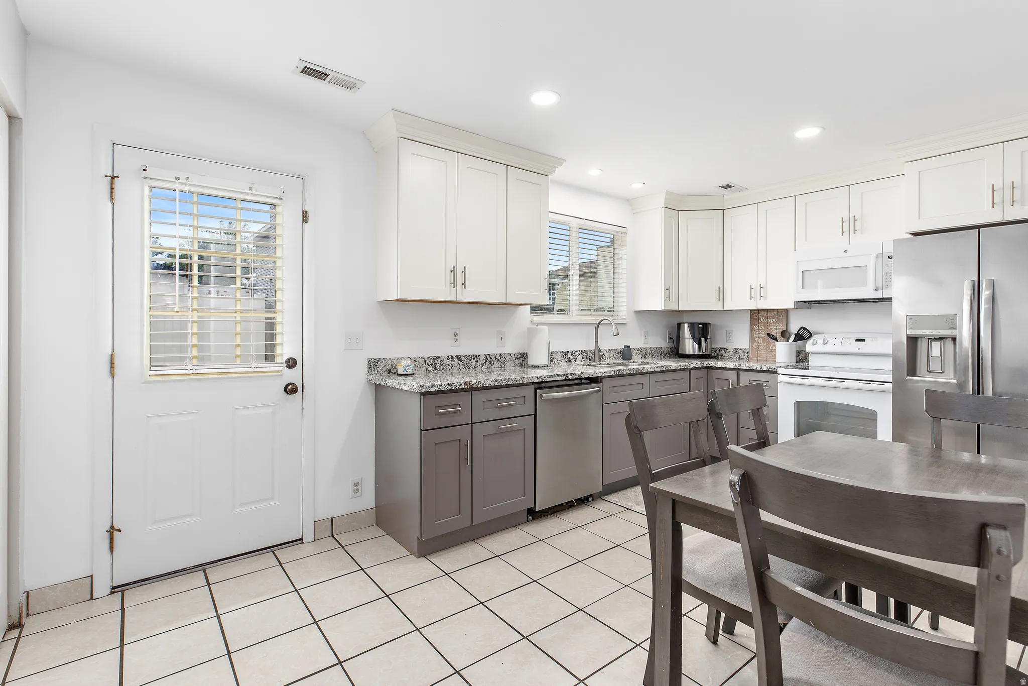 Kitchen featuring two-tone cabinetry with light upper and dark lower cabinets, stainless steel appliances, a white electric range, and light-toned tile flooring
