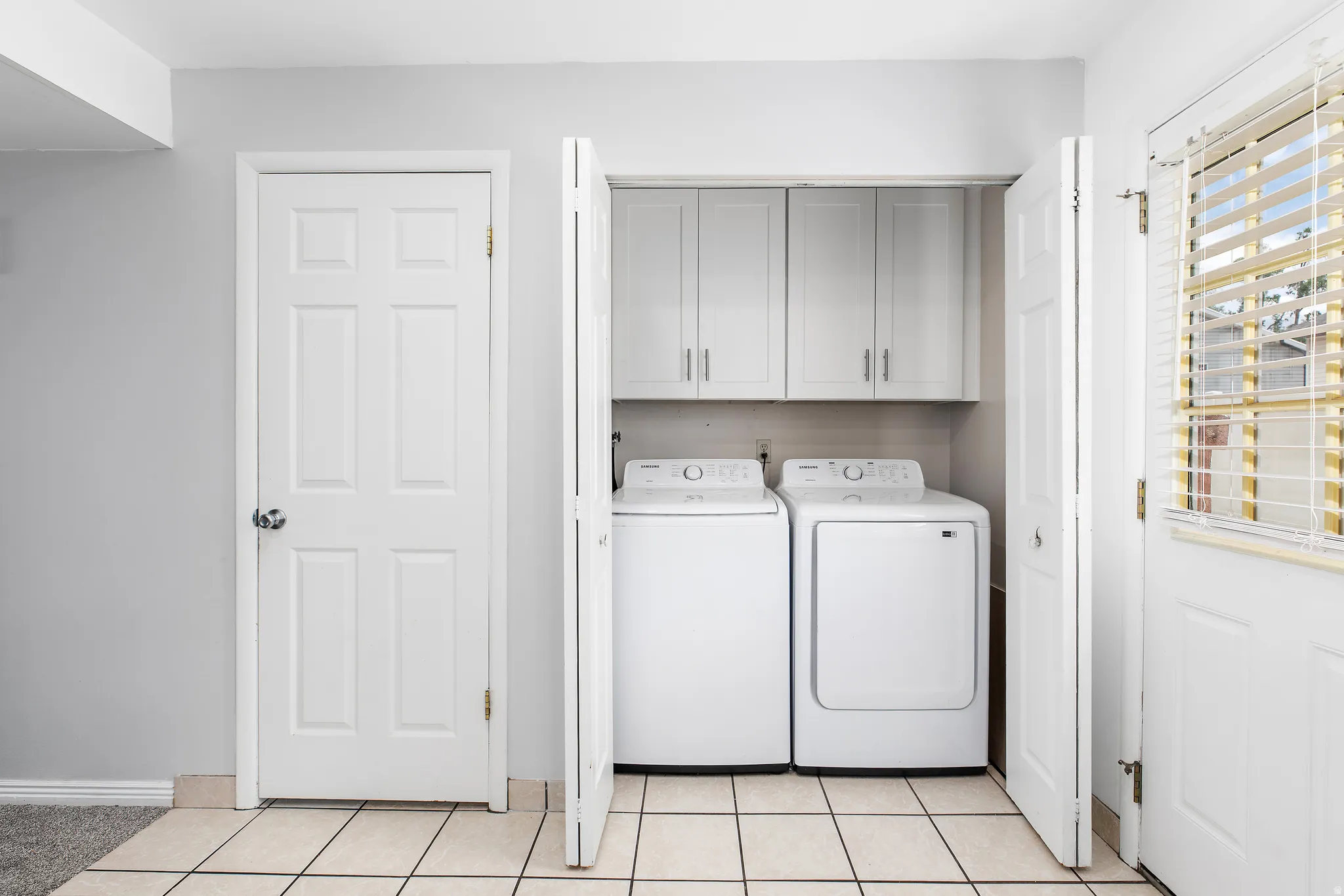 Laundry area featuring white appliances, upper cabinetry, and tile flooring