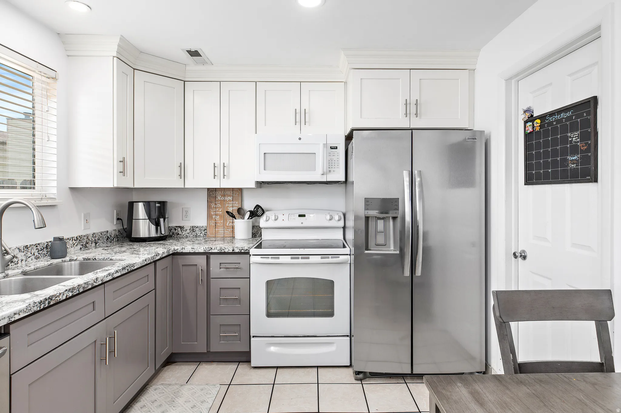 Kitchen featuring two-tone cabinetry with upper white shaker-style doors and lower gray shaker-style doors, granite-style countertops, stainless steel side-by-side refrigerator, white range, and white microwave