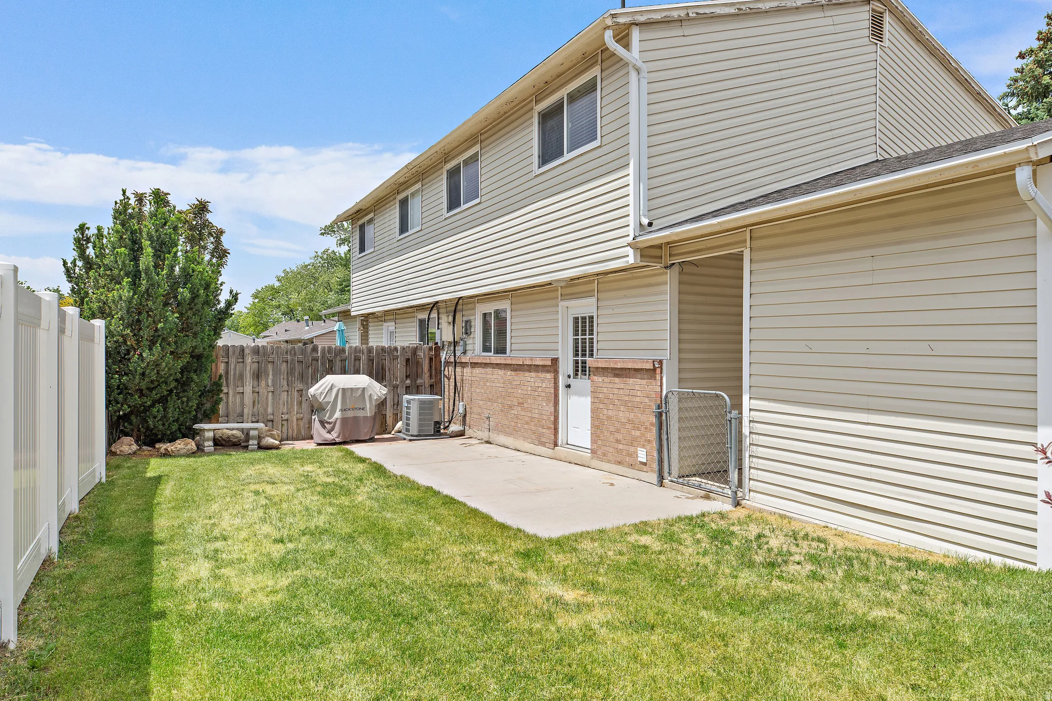 Expansive grass lawn with a concrete patio, bordered by a white vinyl fence and a wood plank fence