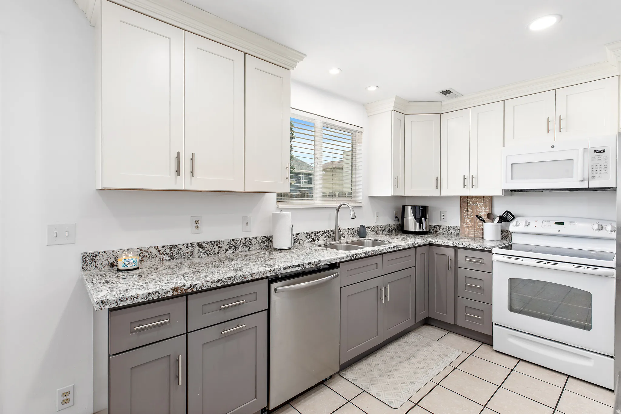 Kitchen featuring two-tone cabinetry with white upper cabinets and gray lower cabinets, granite countertops, stainless steel dishwasher, white range with overhead microwave, and recessed lighting
