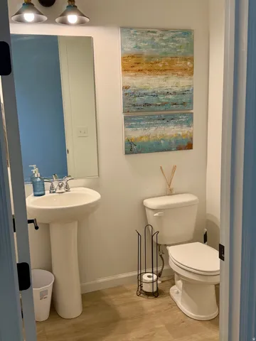 Pedestal sink with chrome faucet, wall-mounted mirror, and wood-finish flooring