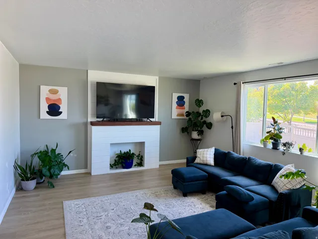 Spacious living area featuring light wood-finish flooring, a contemporary fireplace with a wood mantle and shiplap facade, and large picture windows