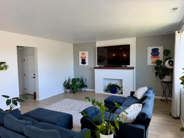 Living area featuring light wood-finish flooring, a contemporary fireplace with a wood mantle, and a recessed fireplace opening