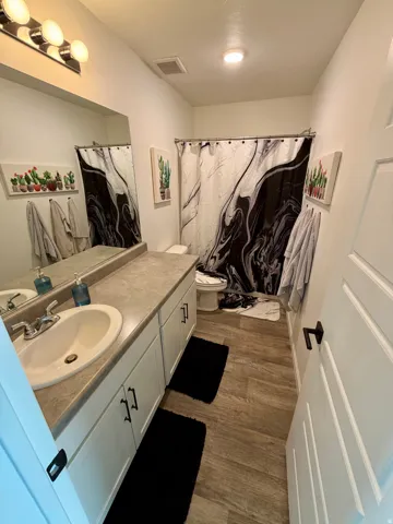 Bathroom featuring an extended single vanity with white cabinetry, a large mirror, a chrome three-bulb vanity light, and wood-finish flooring