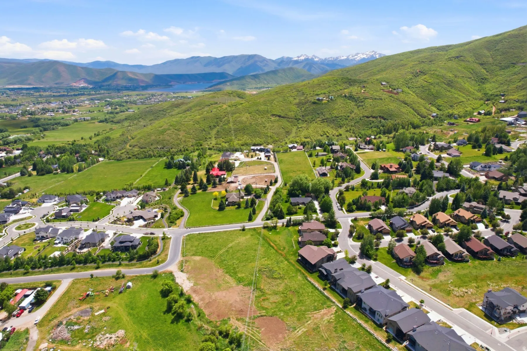 Expansive residential development featuring paved roads and established homes, surrounded by green hillsides and distant mountains with snow-capped peaks