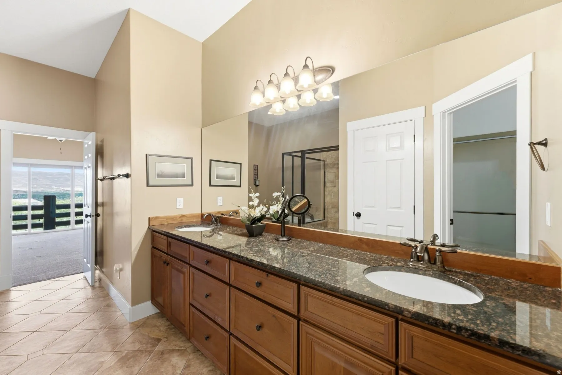 Bathroom featuring a long dual-sink vanity with a dark speckled countertop, light wood cabinetry, and a large mirror reflecting the space