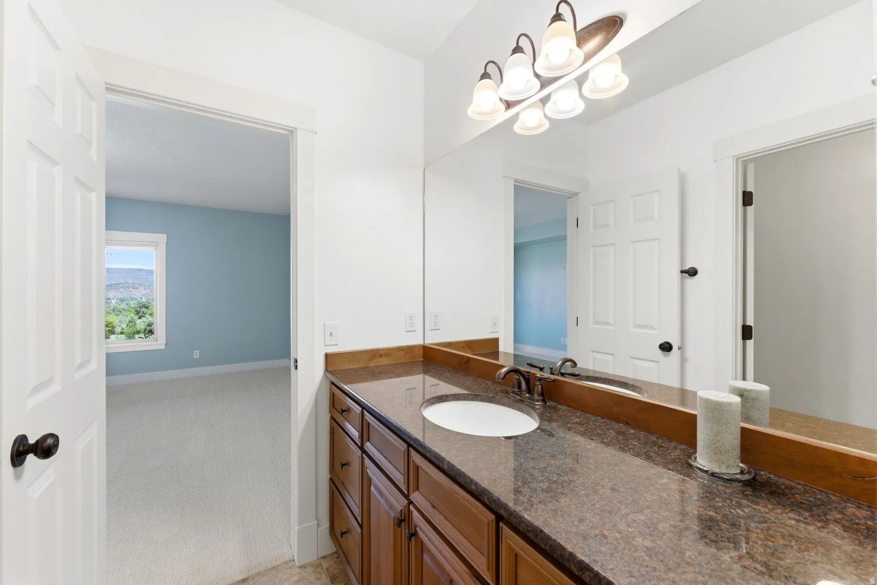 Bathroom vanity featuring a dark granite-style countertop with an undermount sink, wood-finish cabinetry with multiple drawers, and a large mirror