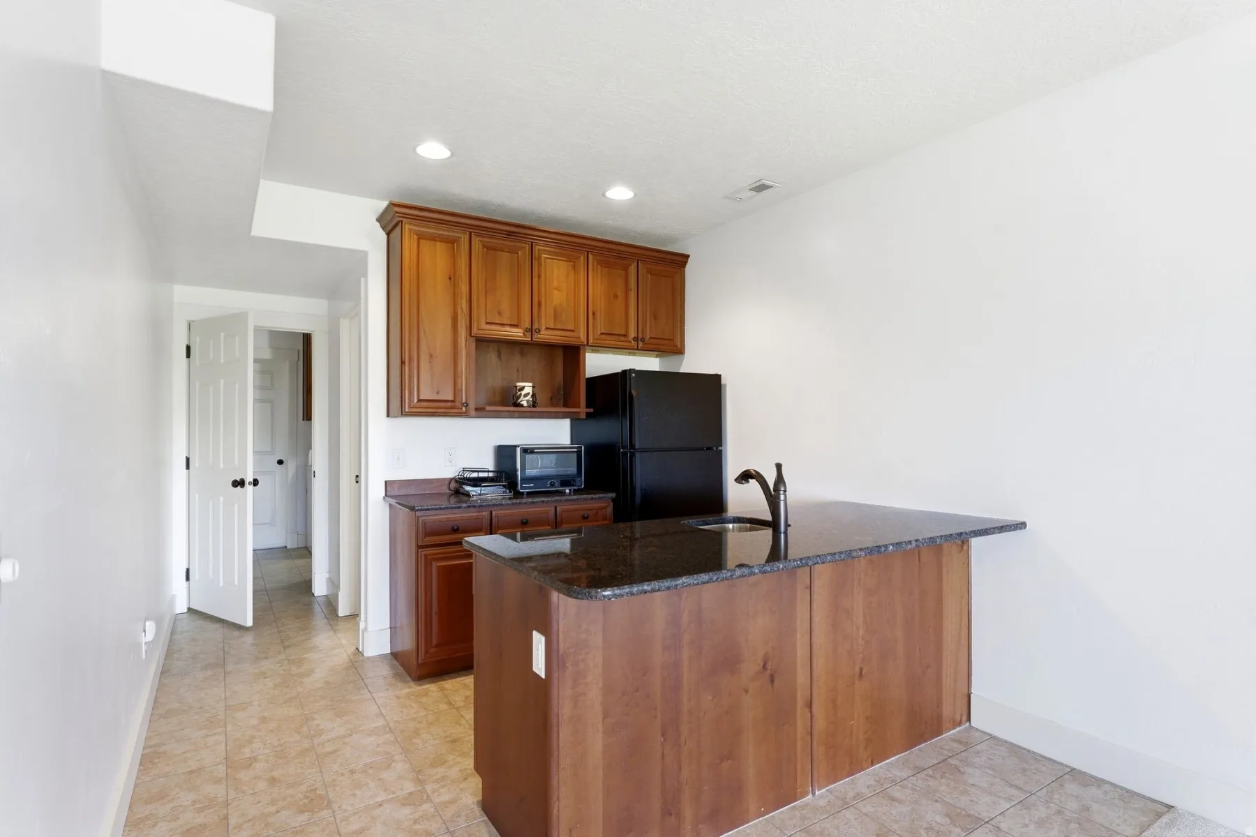 Compact kitchen area featuring wood cabinetry, a dark countertop, an integrated sink, and an included refrigerator