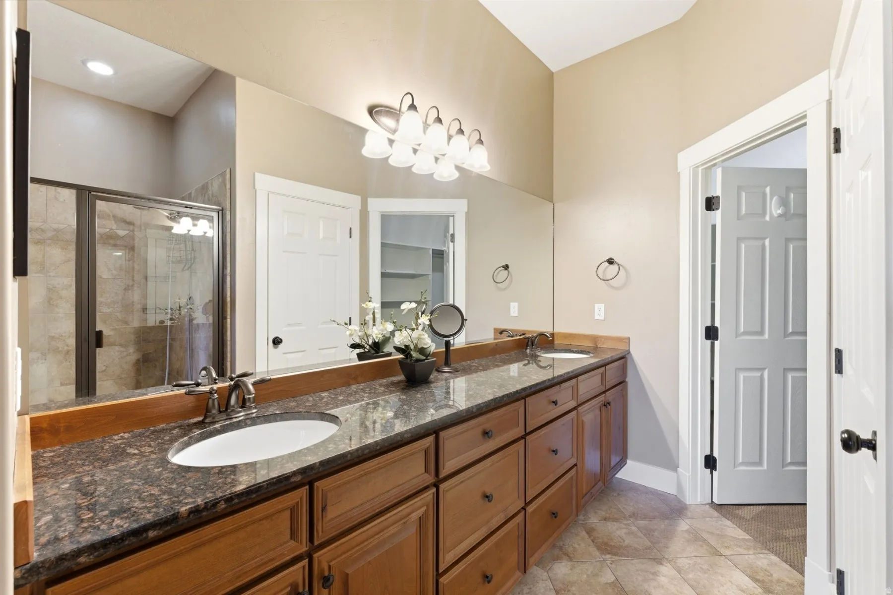 Bathroom vanity featuring a dark stone countertop with dual undermount sinks, wood cabinetry, and a full-width mirror