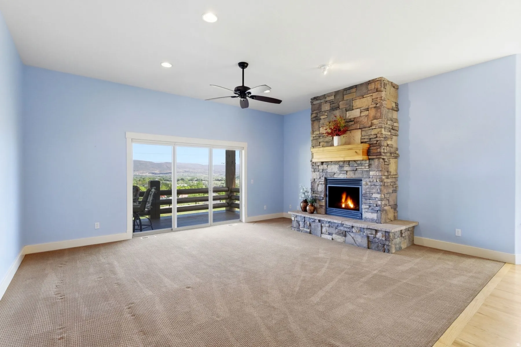 Spacious room featuring a stacked stone fireplace with a substantial wood mantel, a ceiling fan, recessed lighting, and a large sliding glass door opening to an outdoor deck