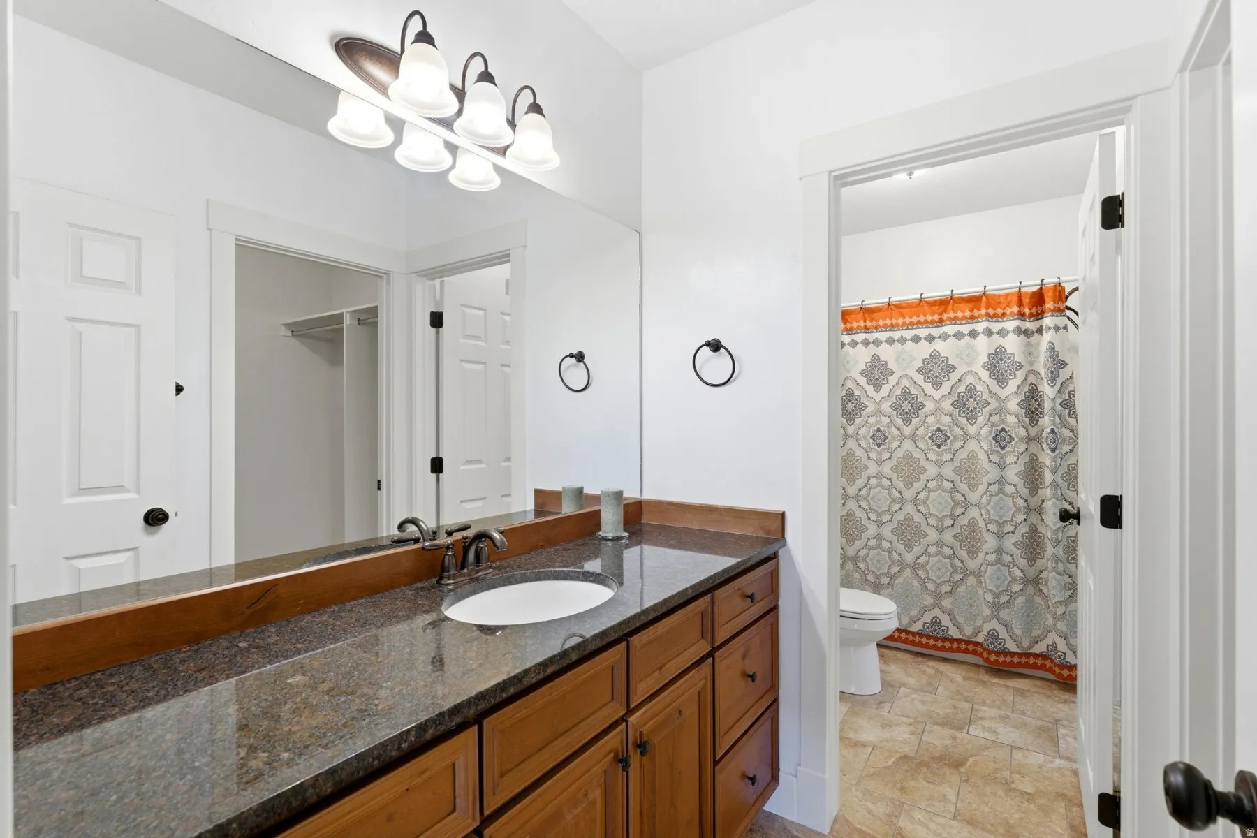 Bathroom featuring a wood vanity with a granite-style countertop, undermount sink, and a framed mirror