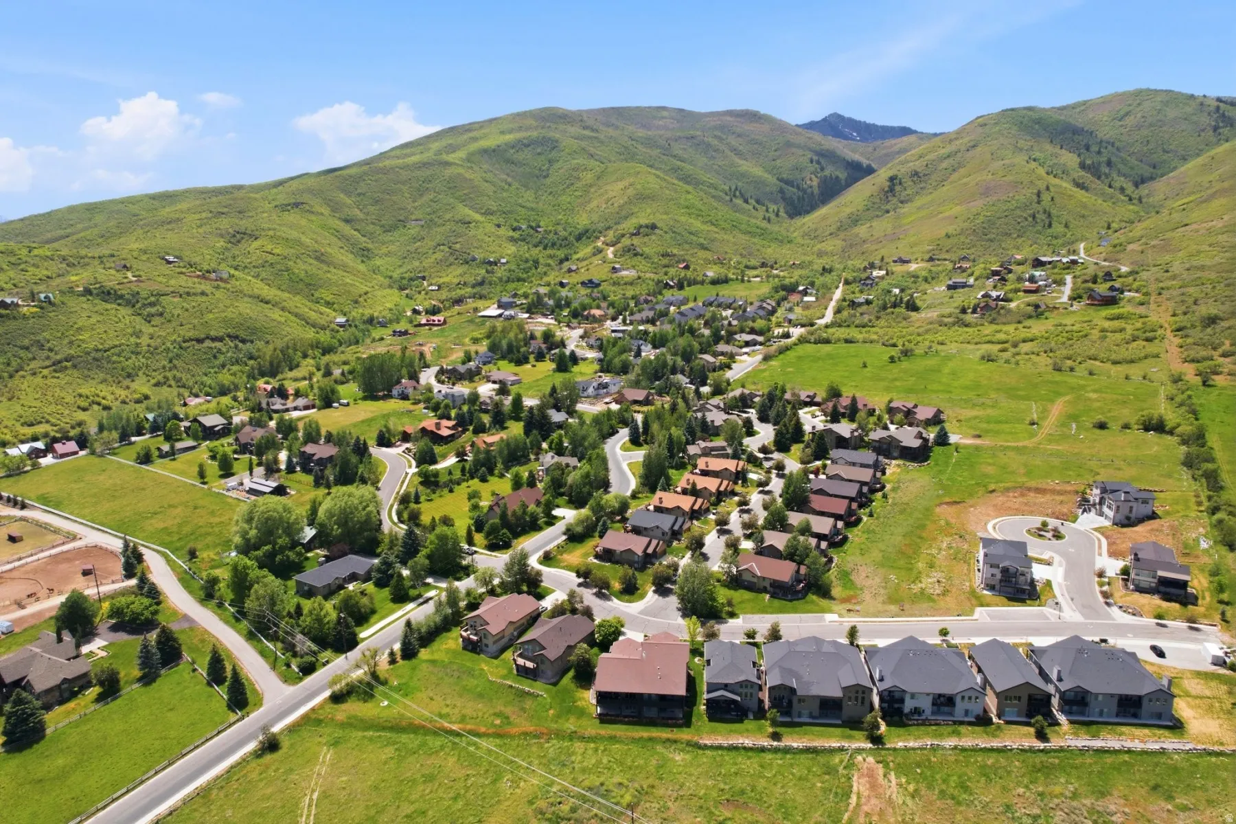 Expansive mountain landscape featuring varied residential architecture, established tree cover, paved roadways, and undeveloped land parcels