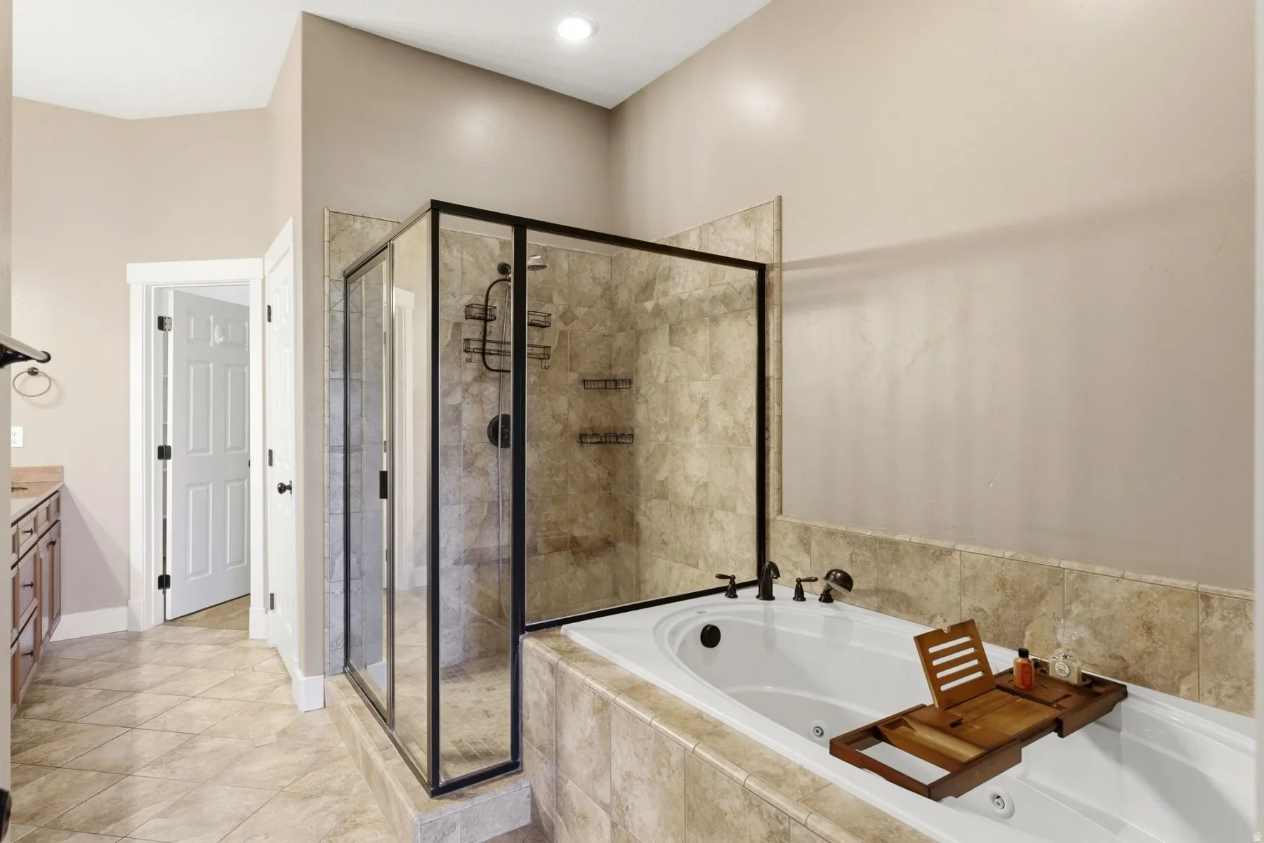 Spacious bathroom featuring a jetted soaking tub, walk-in shower with black-framed glass enclosure, and stone-look tiled flooring