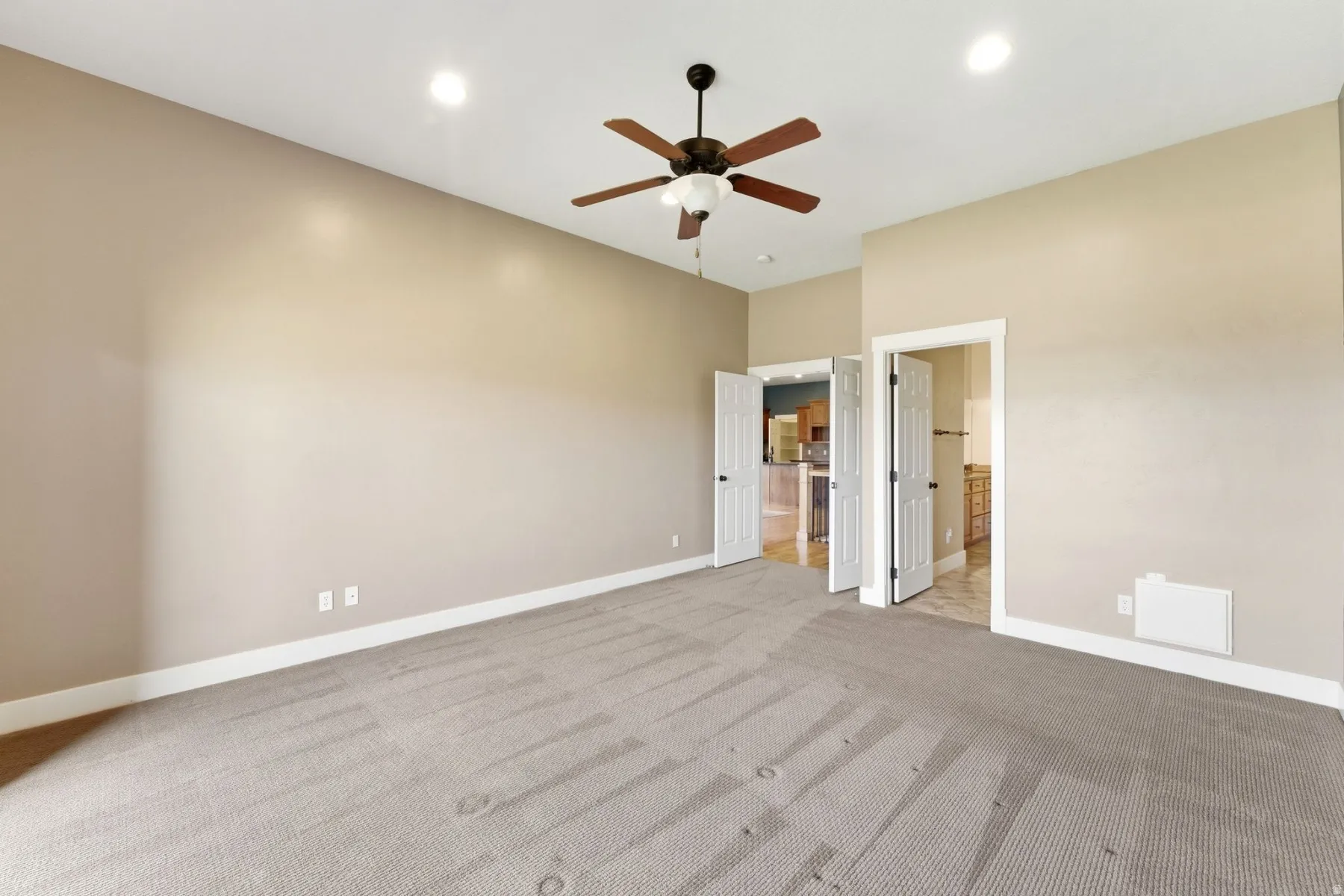Spacious carpeted room featuring a ceiling fan with light fixture, recessed lighting, and multiple doorways