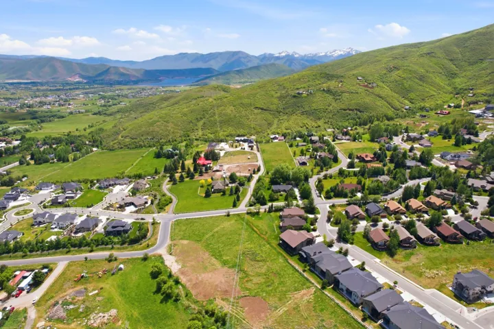Expansive residential development featuring paved roads and established homes, surrounded by green hillsides and distant mountains with snow-capped peaks