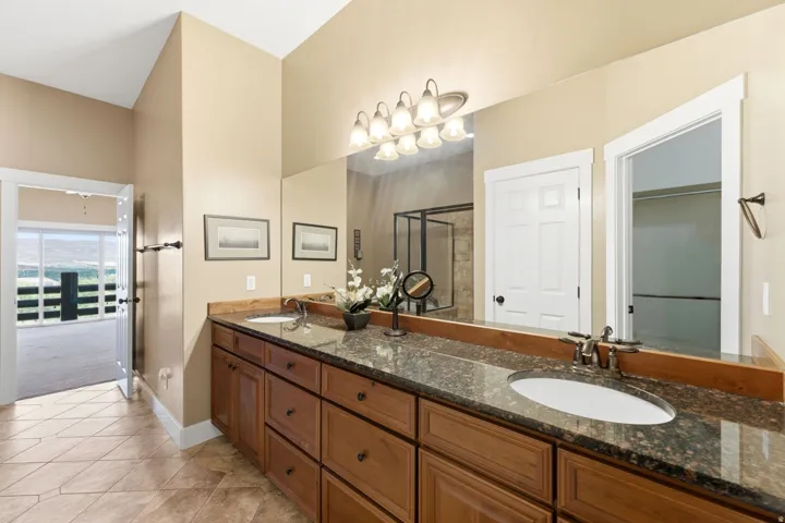 Bathroom featuring a long dual-sink vanity with a dark speckled countertop, light wood cabinetry, and a large mirror reflecting the space