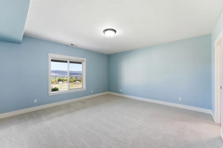 Spacious room with light blue walls, soft neutral carpeting, and a large window offering expansive distant scenery