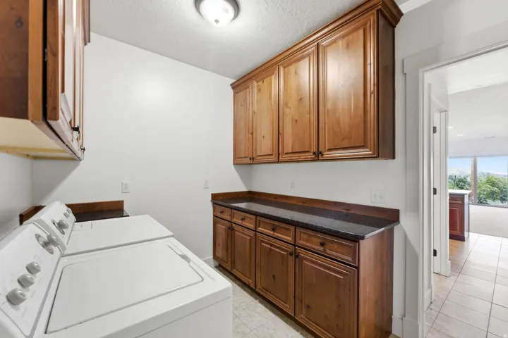 Dedicated laundry room featuring ample wood cabinetry, dark countertops, and tile flooring
