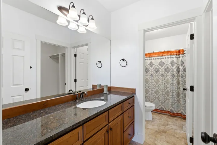 Bathroom featuring a wood vanity with a granite-style countertop, undermount sink, and a framed mirror