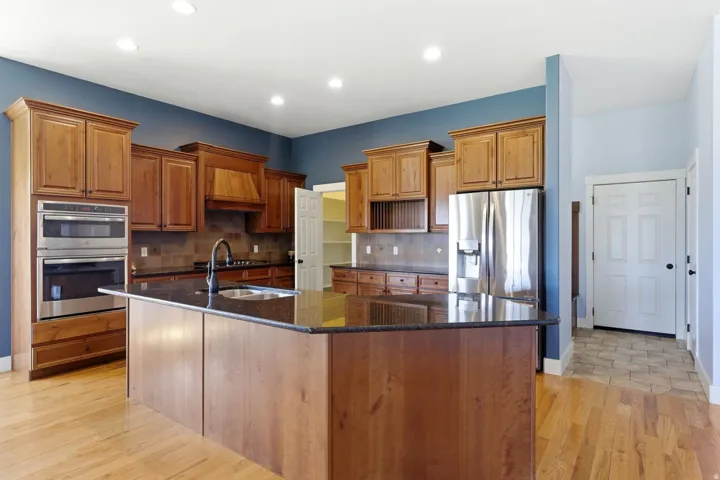 Kitchen featuring a large central island with a dark countertop, wood cabinetry, stainless steel appliances, and wood-finish flooring