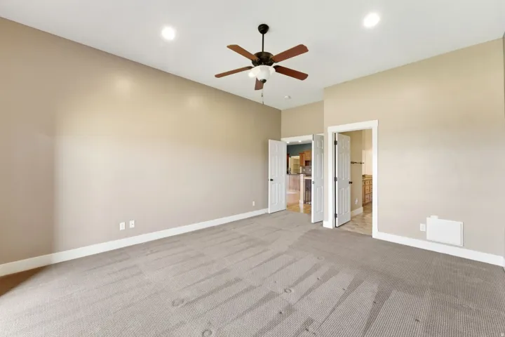 Spacious carpeted room featuring a ceiling fan with light fixture, recessed lighting, and multiple doorways