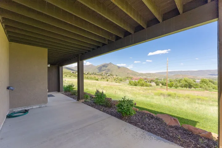 Covered concrete patio with a stucco exterior, dark wood ceiling beams, and a landscaped rock bed