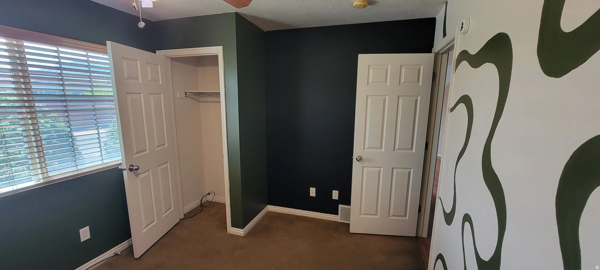 Room featuring a window with horizontal blinds, built-in closet with shelving, a ceiling fan, and distinct wall treatments including a dark accent wall and a patterned wall