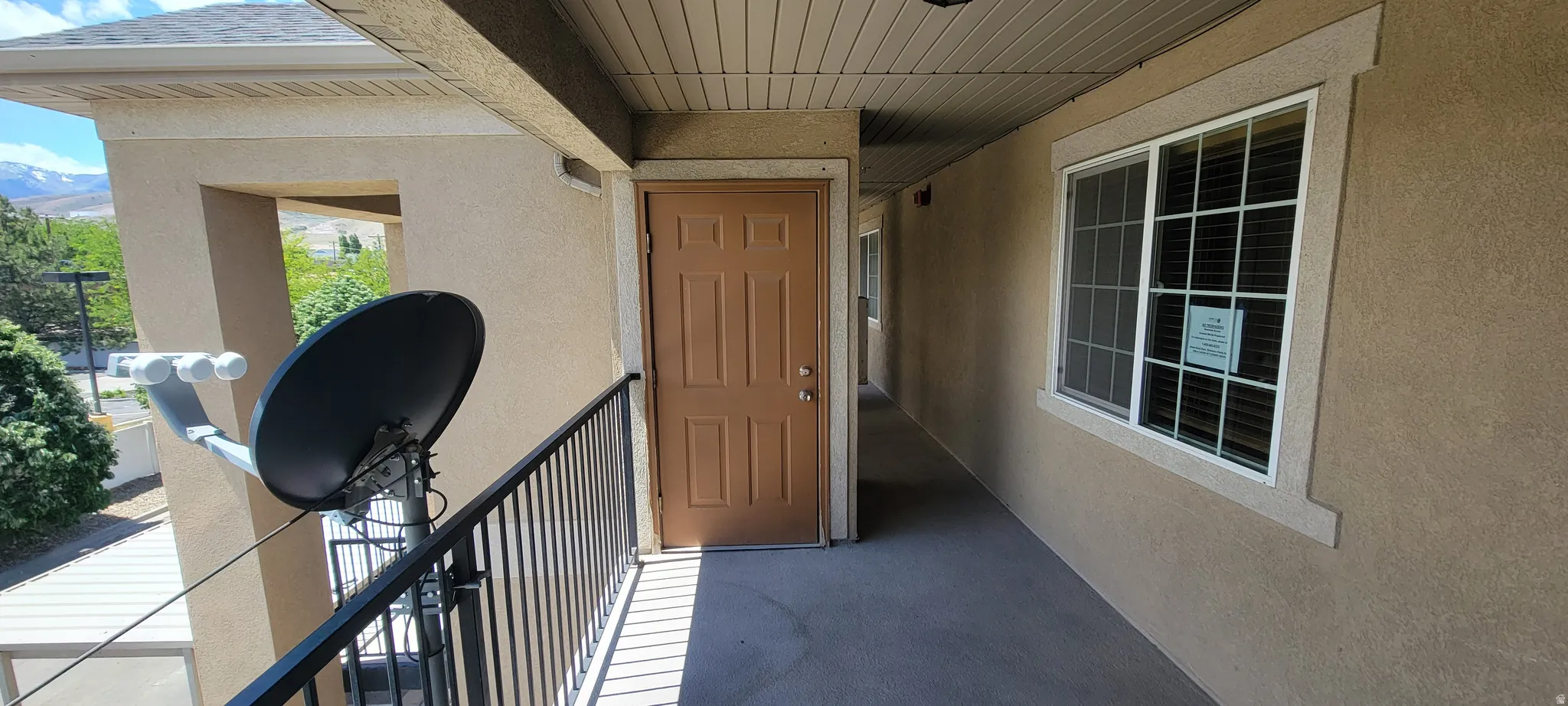 Exterior balcony entry featuring a light brown paneled door, stucco finish, and white-framed window with blinds