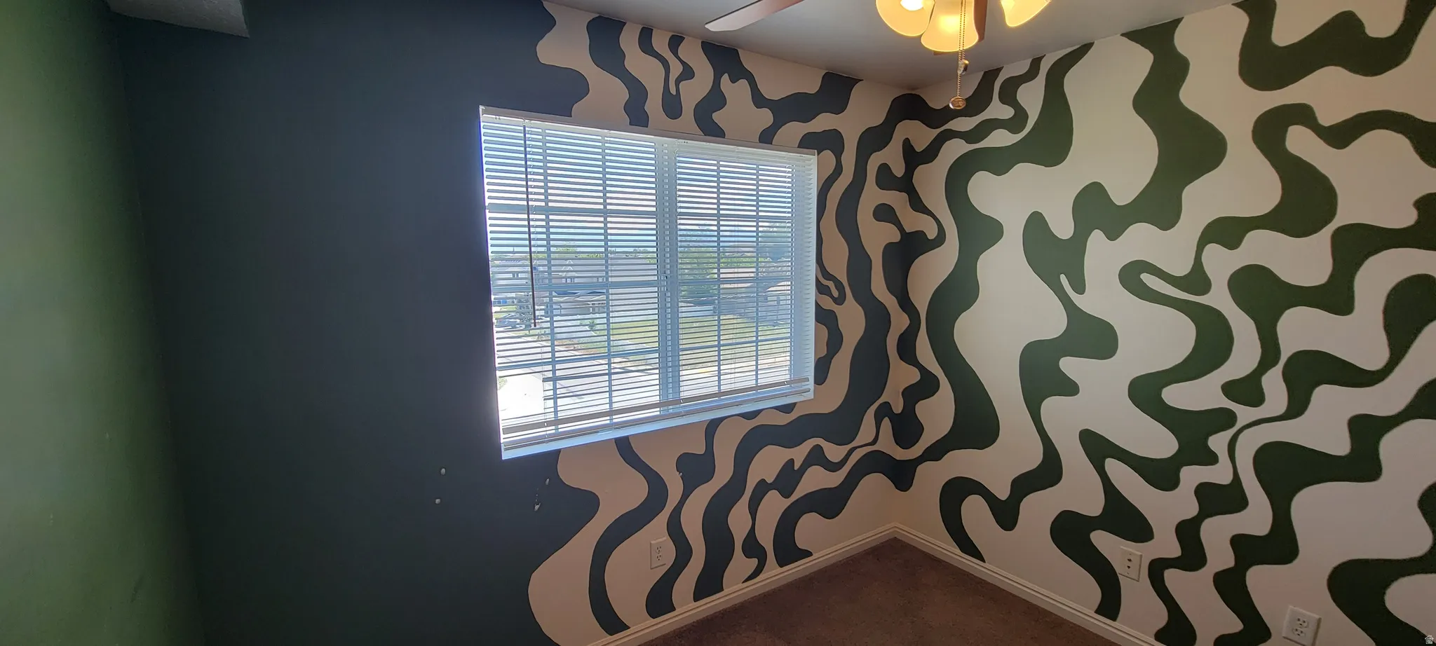 Room featuring a window with horizontal blinds, patterned walls, a ceiling fan, and carpet flooring