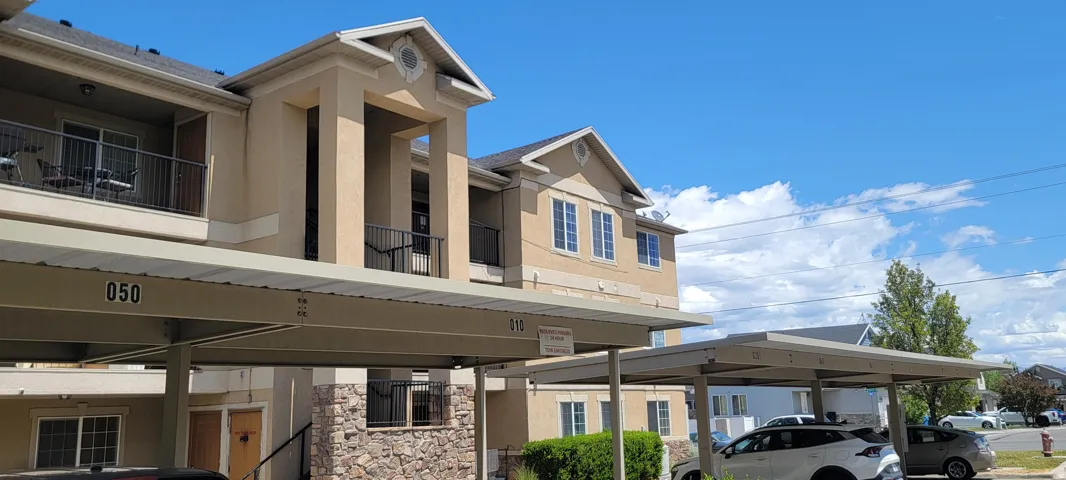 Residential building featuring covered parking, stucco exterior, stone facade accents, multiple windows, and private balconies with black railings