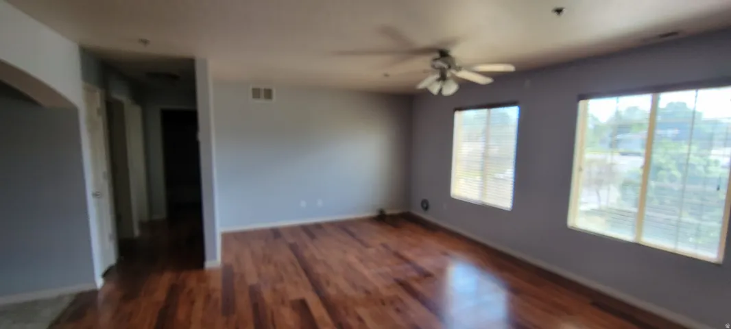 Spacious room featuring wood-finish flooring, light grey walls, and ample natural light from multiple windows