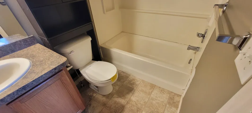 Bathroom featuring a white bathtub and shower surround, a white toilet, and a vanity with a laminate countertop and wood-finish cabinetry