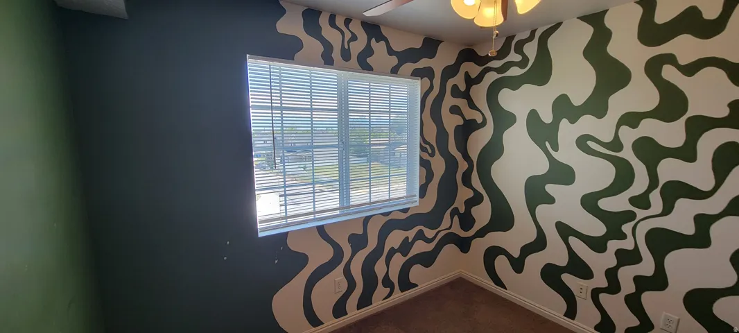 Room featuring a window with horizontal blinds, patterned walls, a ceiling fan, and carpet flooring