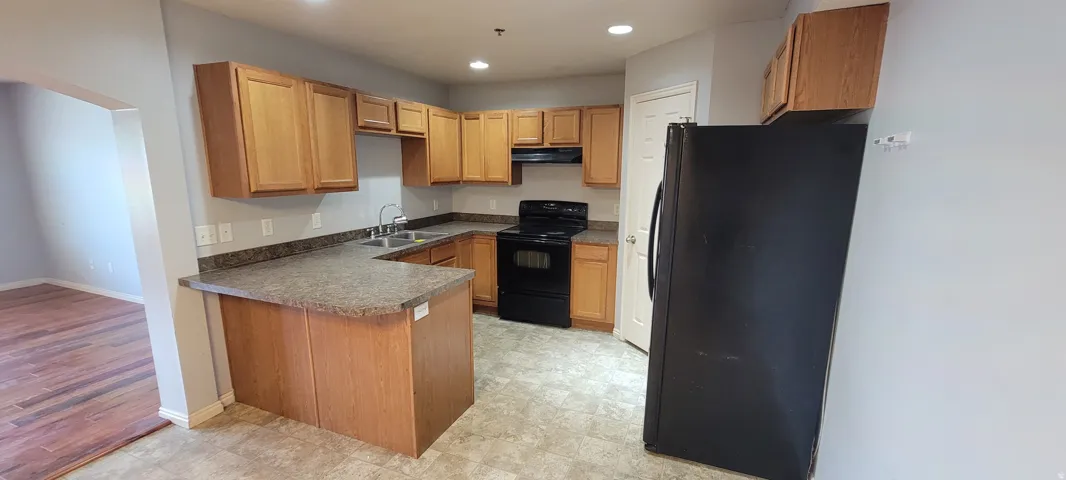Kitchen featuring a U-shaped countertop, wood cabinetry, black appliances, and recessed lighting