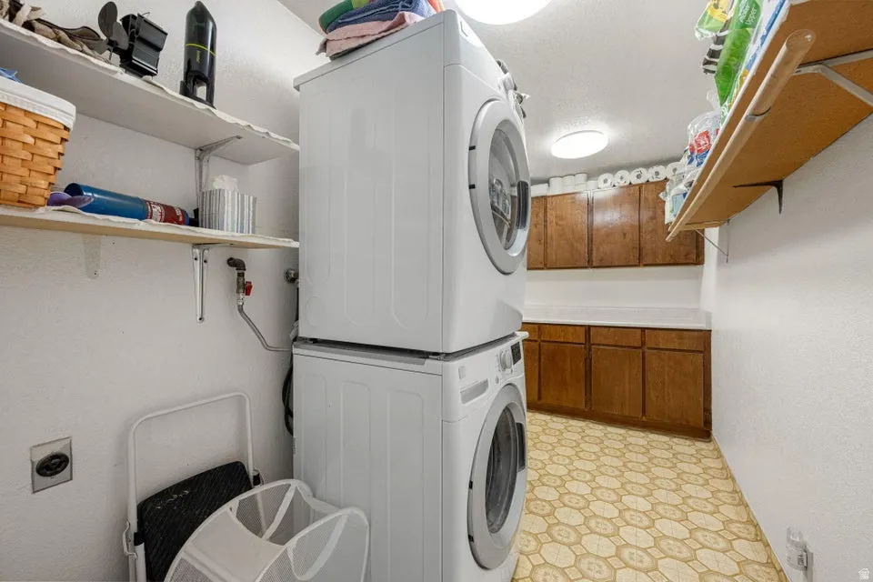 Dedicated laundry area with stacked appliances, overhead shelving, wood-finish cabinetry, countertop space, and patterned flooring