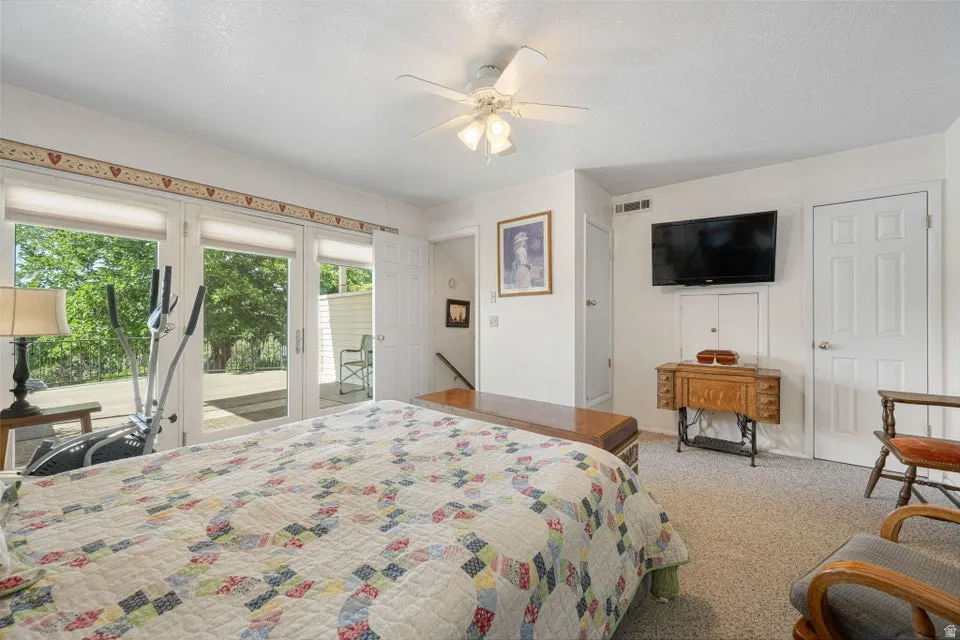 Carpeted room featuring a ceiling fan with integrated lighting, dual French doors opening to an exterior area, and a wall-mounted flat-screen television