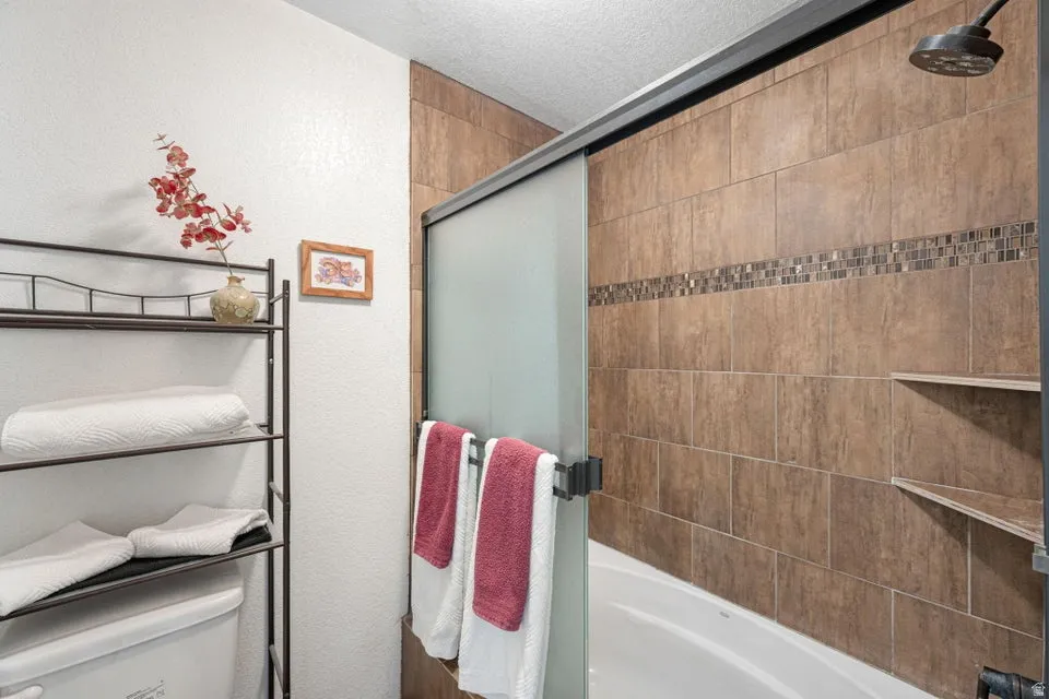 Bathtub with ceramic tile surround, decorative mosaic accent band, and integrated corner shelving