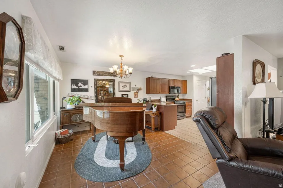 Open concept living area featuring terracotta-style tile flooring and a kitchen with wood-finish cabinetry, black appliances, and a central island