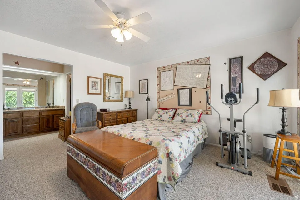 Carpeted room with an open entry to a bathroom featuring a dual vanity with wood-finish cabinetry and an overhead mirror