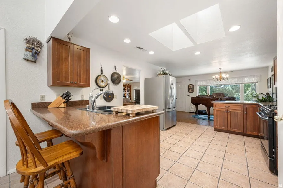 Kitchen featuring recessed lighting, a breakfast bar with seating, a stainless steel sink with a gooseneck faucet, tile flooring, and two skylights