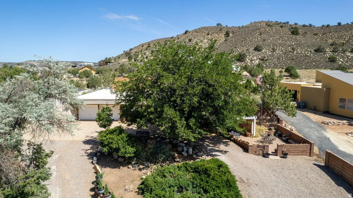 Desert landscape setting featuring a gravel driveway, mature trees, and natural rock elements