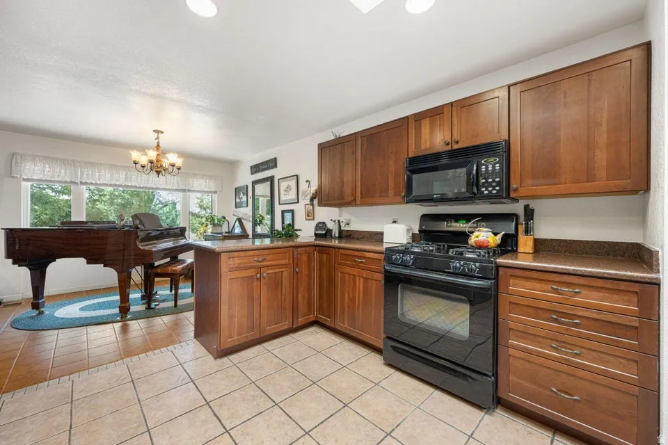 Kitchen featuring tiled flooring, wood cabinetry, dark countertops, a black gas range, and a black built-in microwave